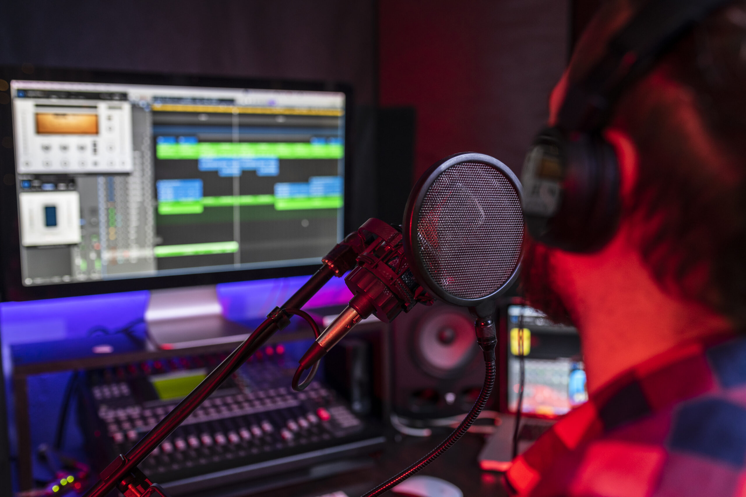 White young man is singing and recording a new track in the stereo studio workplace using song mixer and microphone